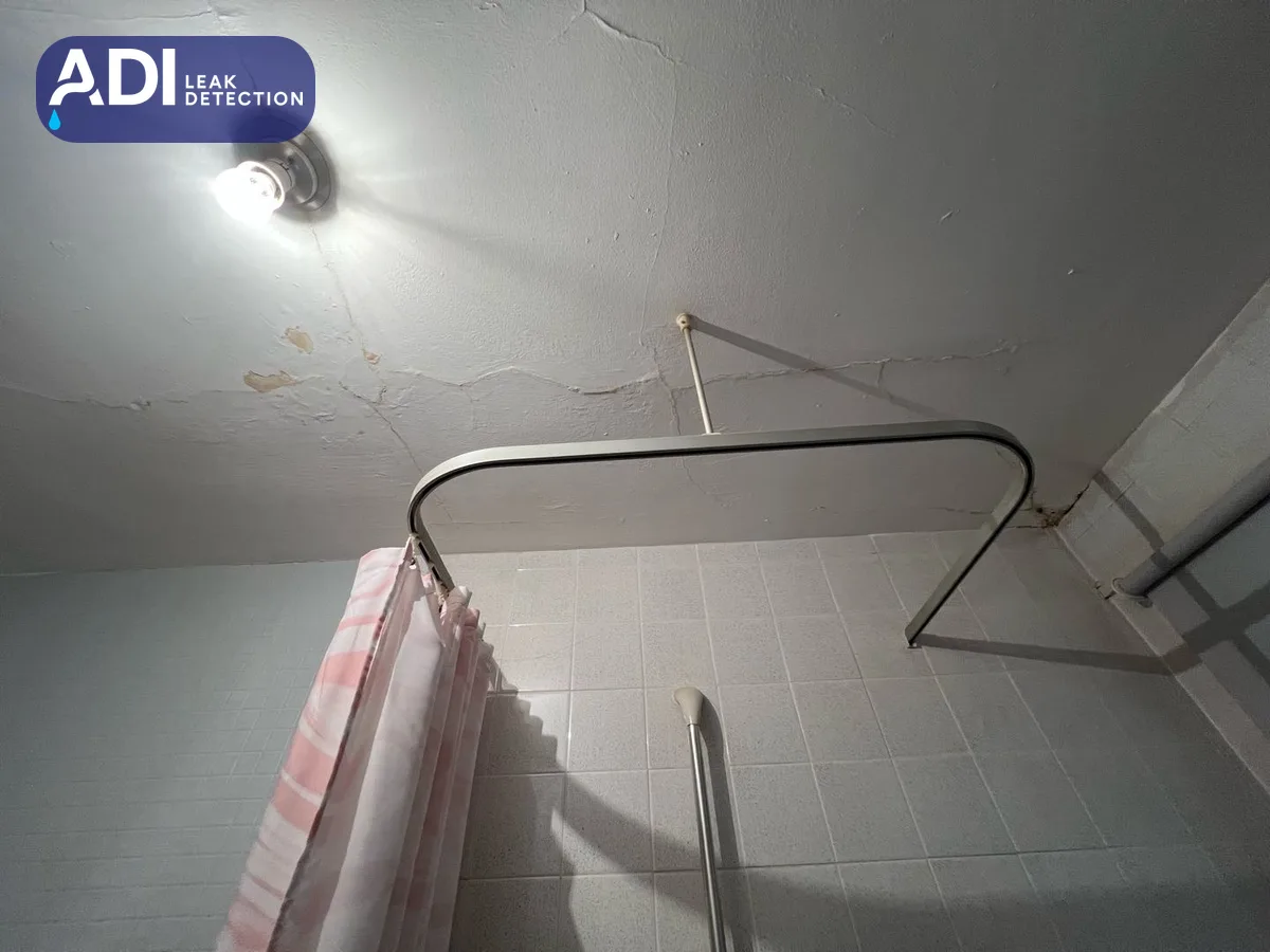A cracked bathroom ceiling above a shower curtain rail